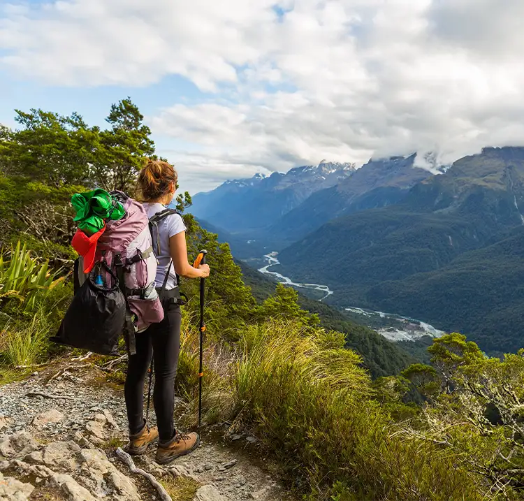 a young woman standing on a hiking path taking in the large mountain view