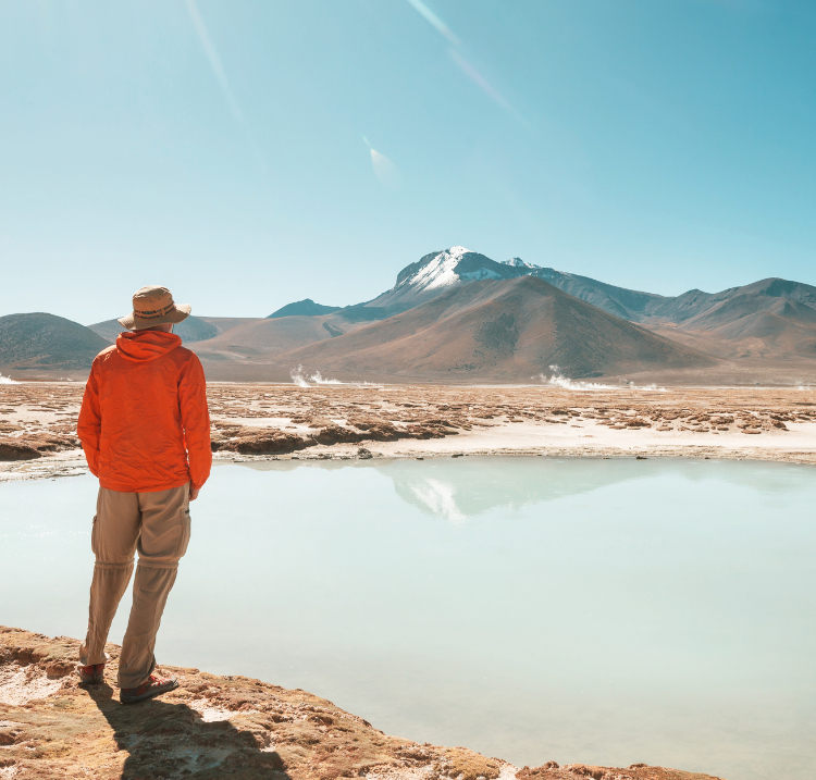 man on a hike next to a beautiful clear pond with mountains in the background