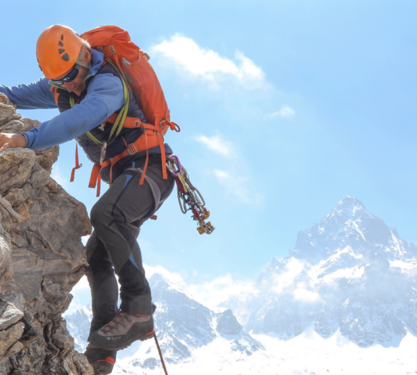 mountain climber scaling down a huge boulder with snowy mountains in the background